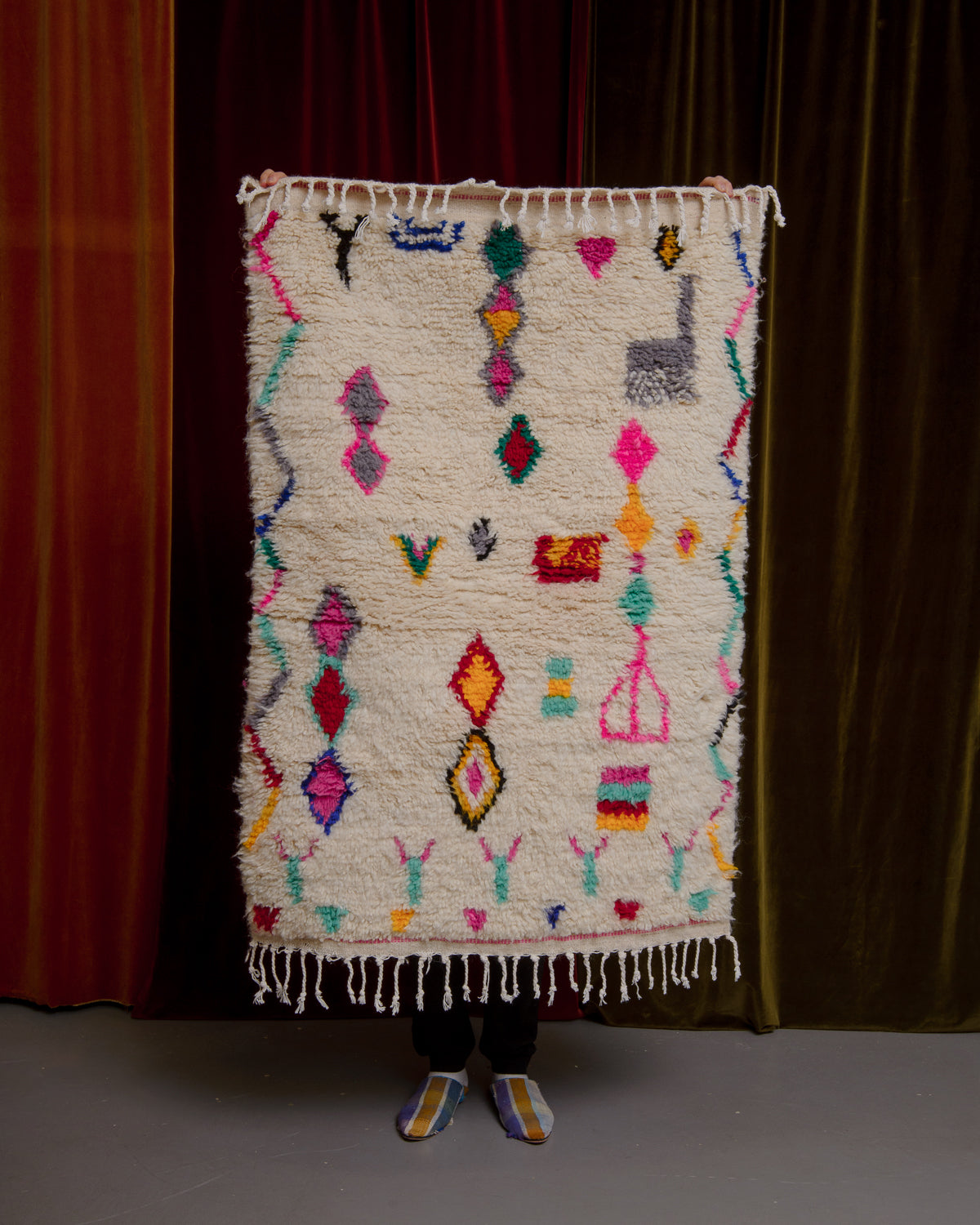 Azilal rug held in front of velvet curtains. 