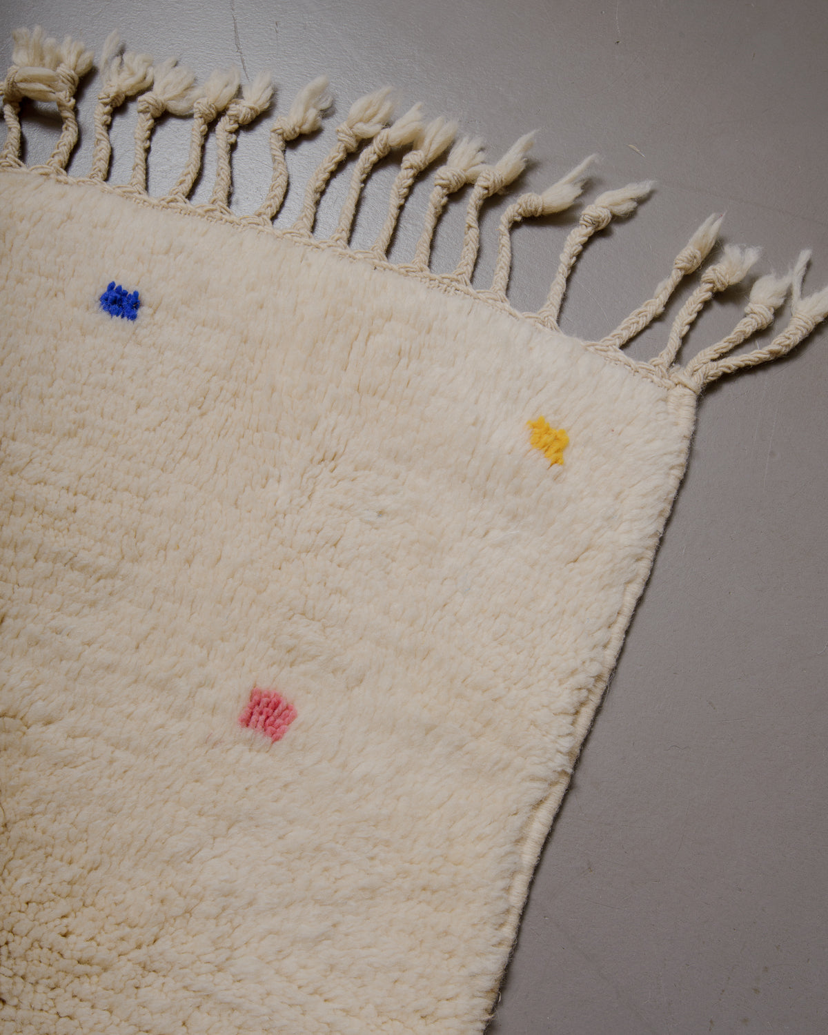 Corner of cream wool rug with colourful polka dots and natural wool tassels.