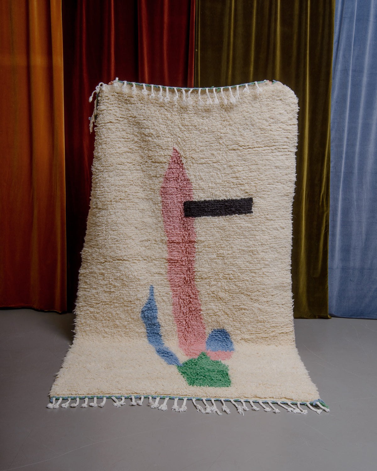 Azilal rug held in front of velvet curtains. 