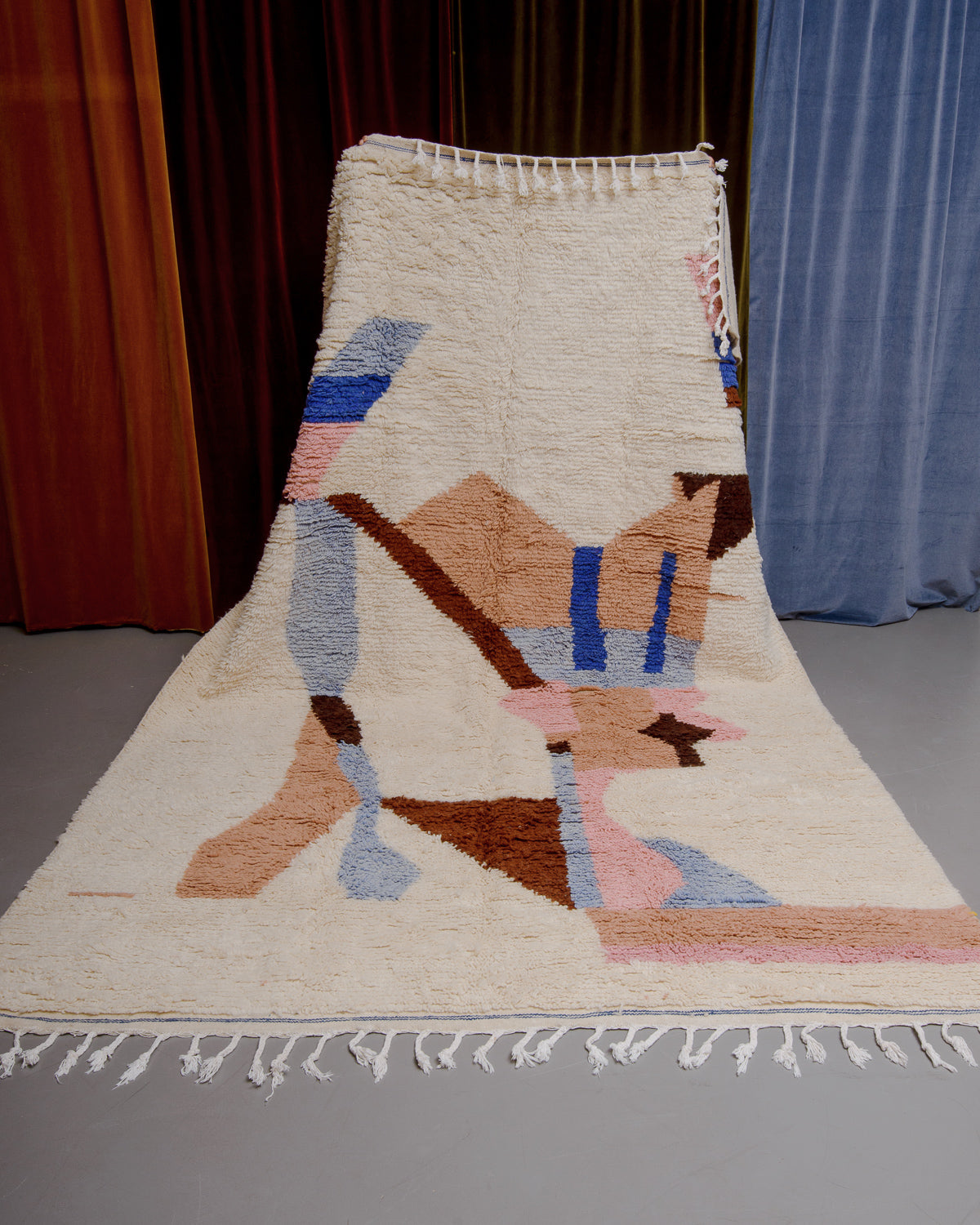Azilal rug held in front of velvet curtains. 