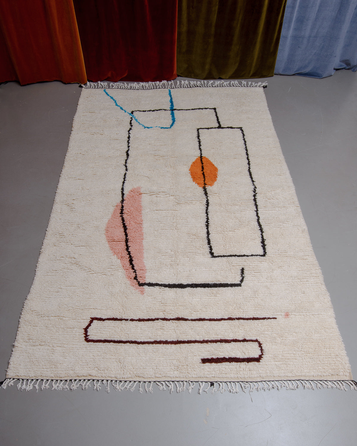 Azilal rug featuring colourful design on a grey floor in front of curtains.