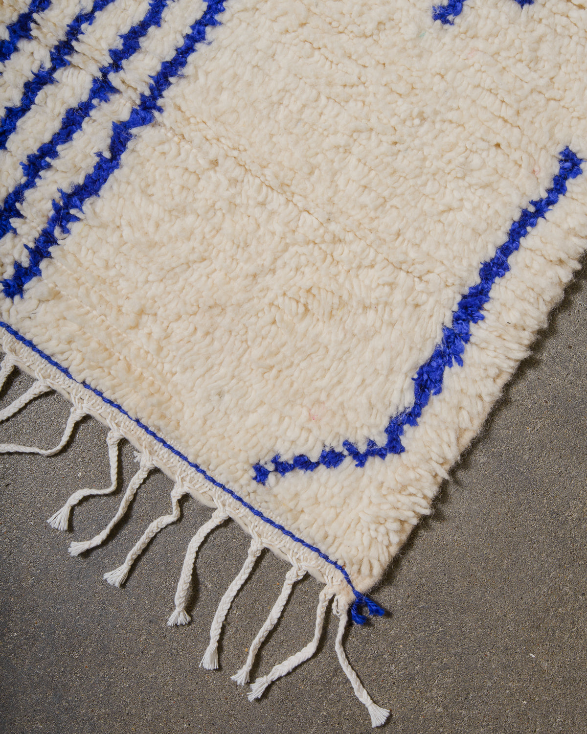 Edge of Azilal rug with white cotton tassels along the edge on cement floor.