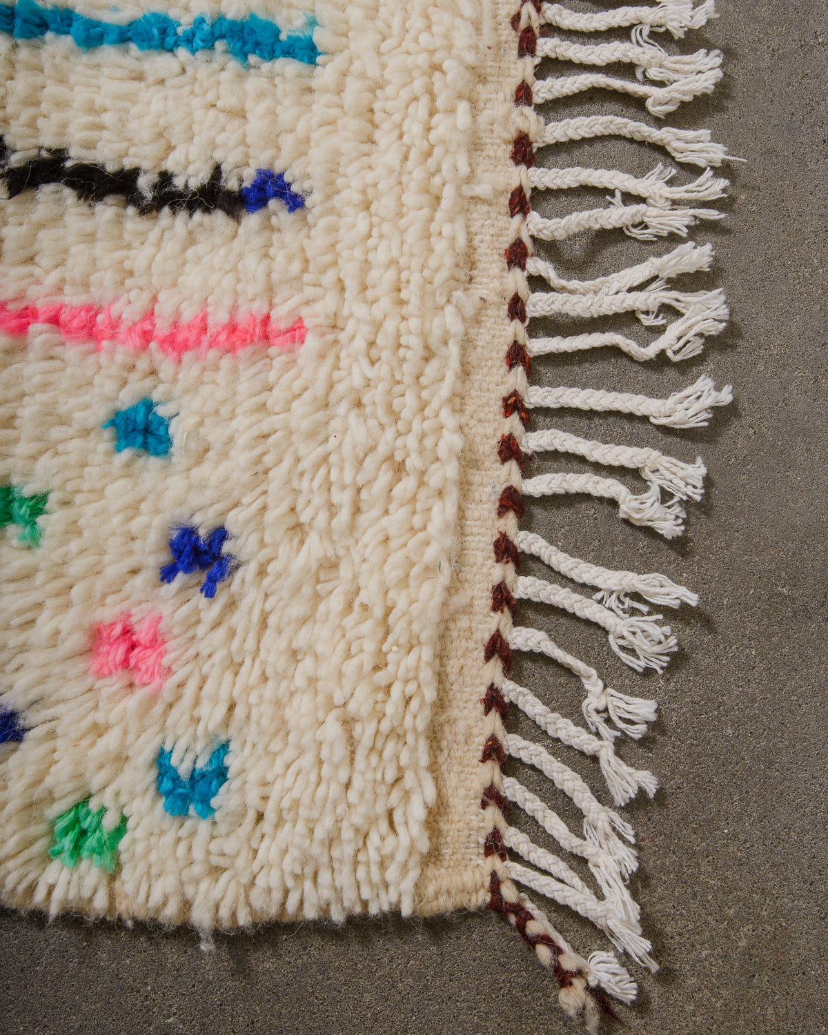 Corner of Azilal run with cream wool and white cotton across the edge and brown trim.