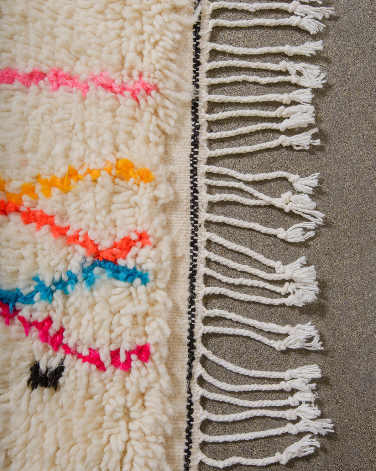 Edge of Azilal rug with black detail and white cotton tassels along the edge.