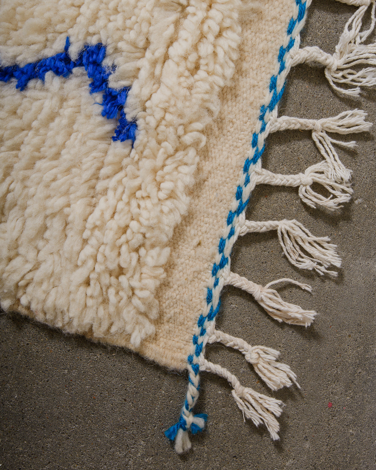 Corner of Azilal run with cream wool and colourful design and white cotton tassels across the edge with blue trim.
