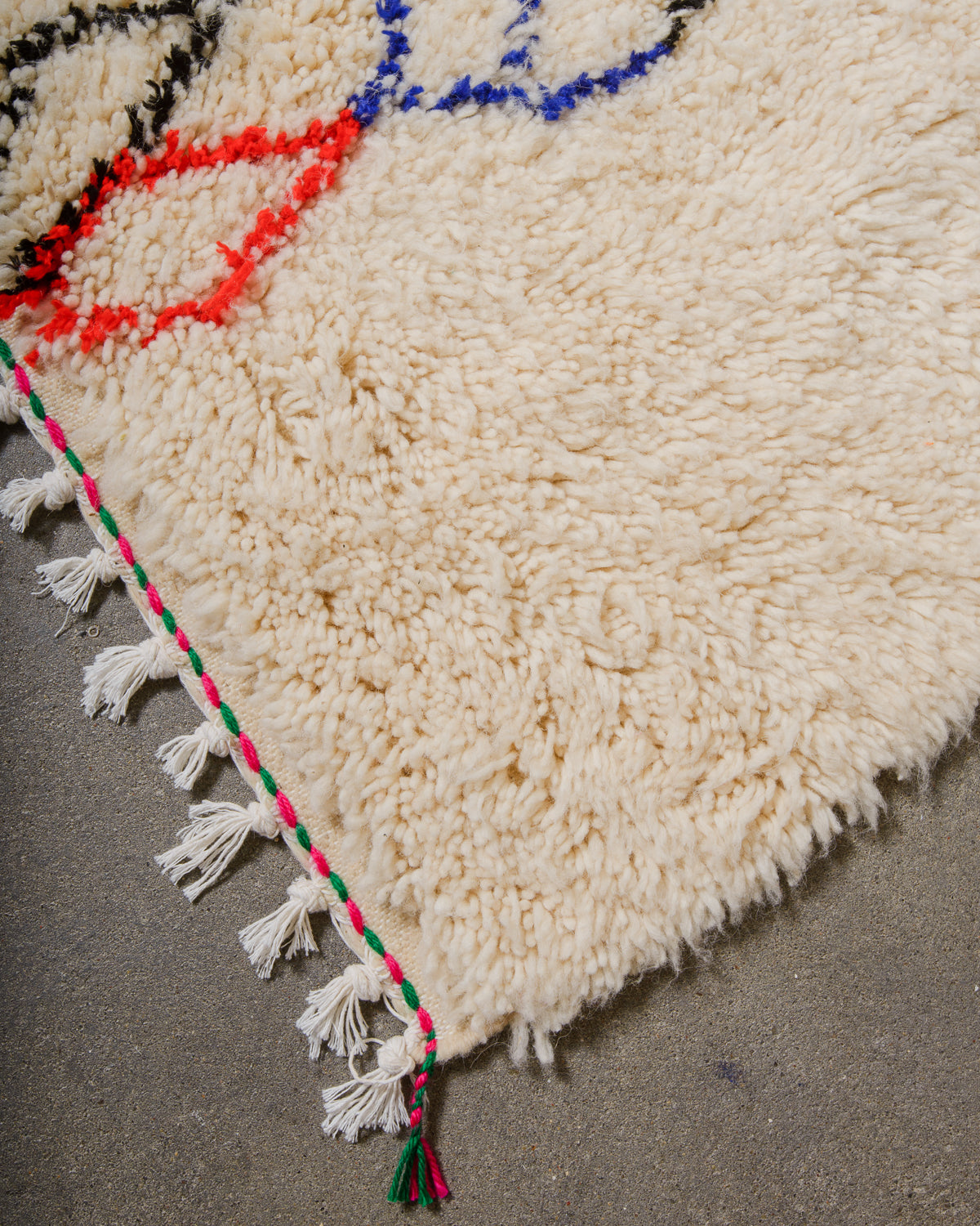 Corner of Azilal run with cream wool and colourful design and white cotton tassels across the edge with pink and green trim.