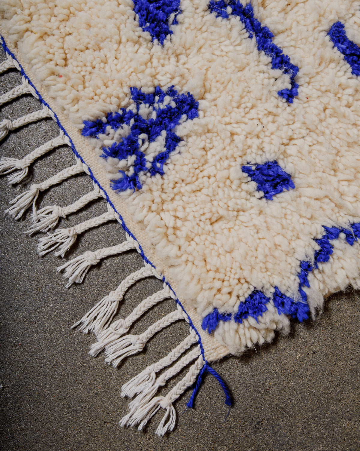 Close-up of a cream and blue patterned rug with tassels on a dark surface
