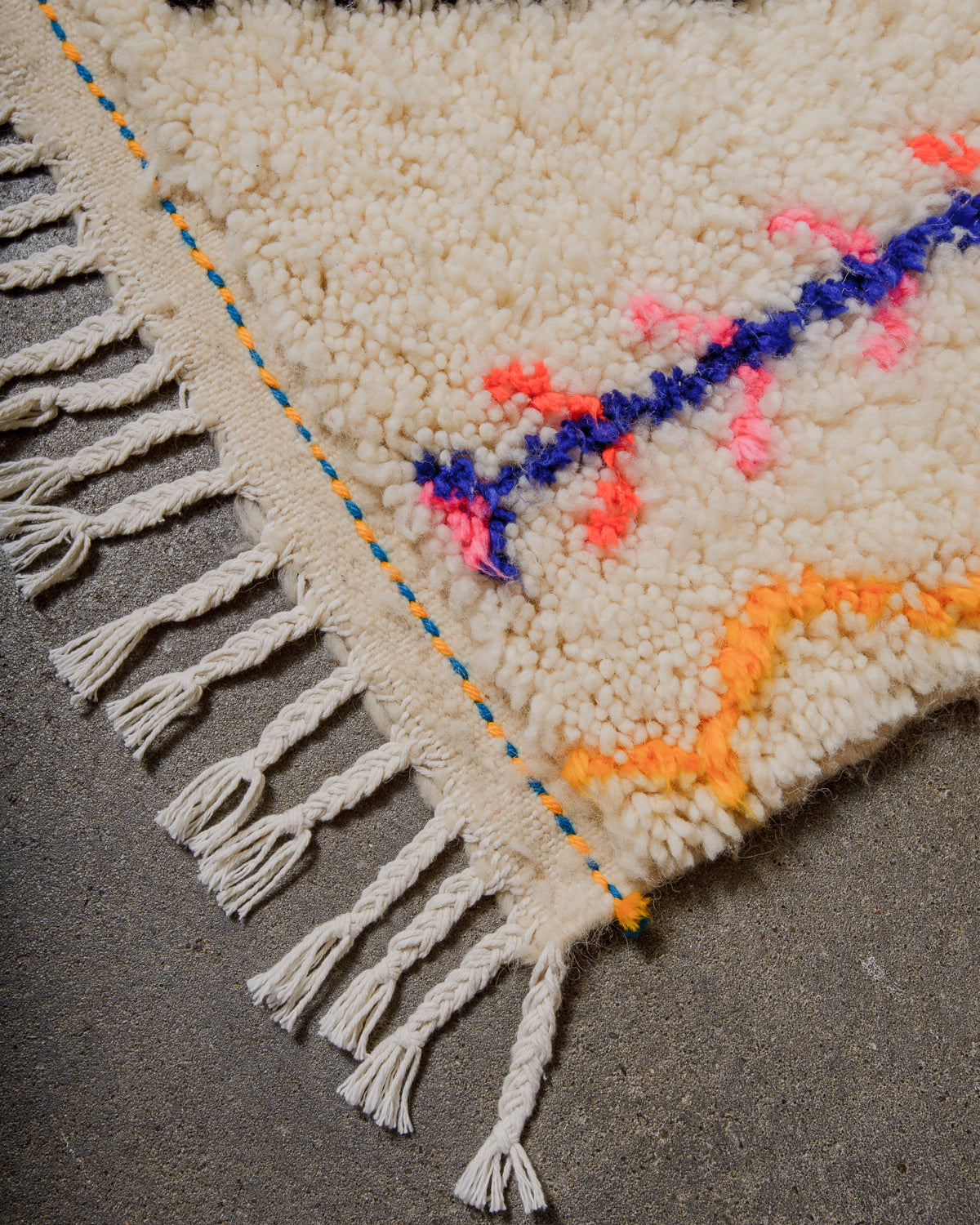 Close-up of a textured rug with colorful patterns and fringes on a gray surface