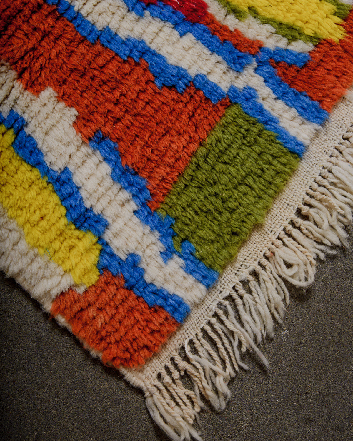 Corner of colourful woven rug with geometric pattern on a concrete surface