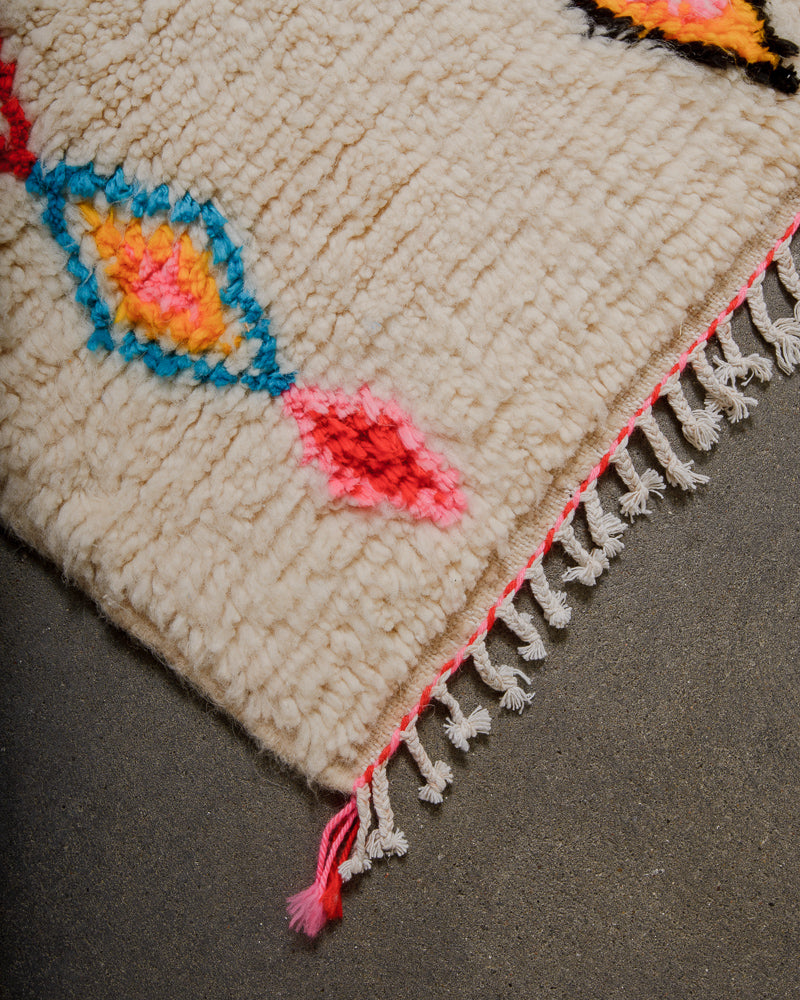 Corner of an azilal rug with pink and red details and white cotton tassels. 
