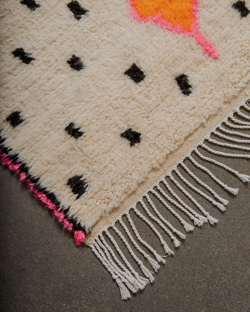 Azilal rug with black dot pattern, pink edge and white cotton tassels on concrete floor. 