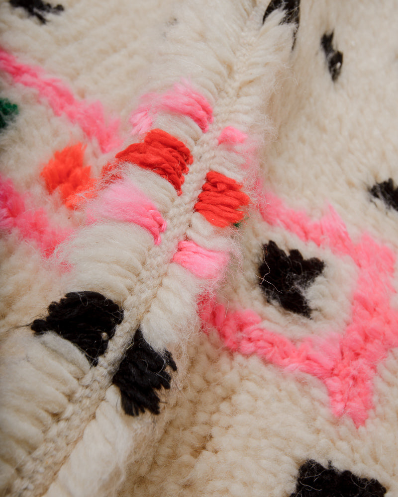 Close-up of Azilal rug with black dot pattern and pink and red motif on a cream wool background. 