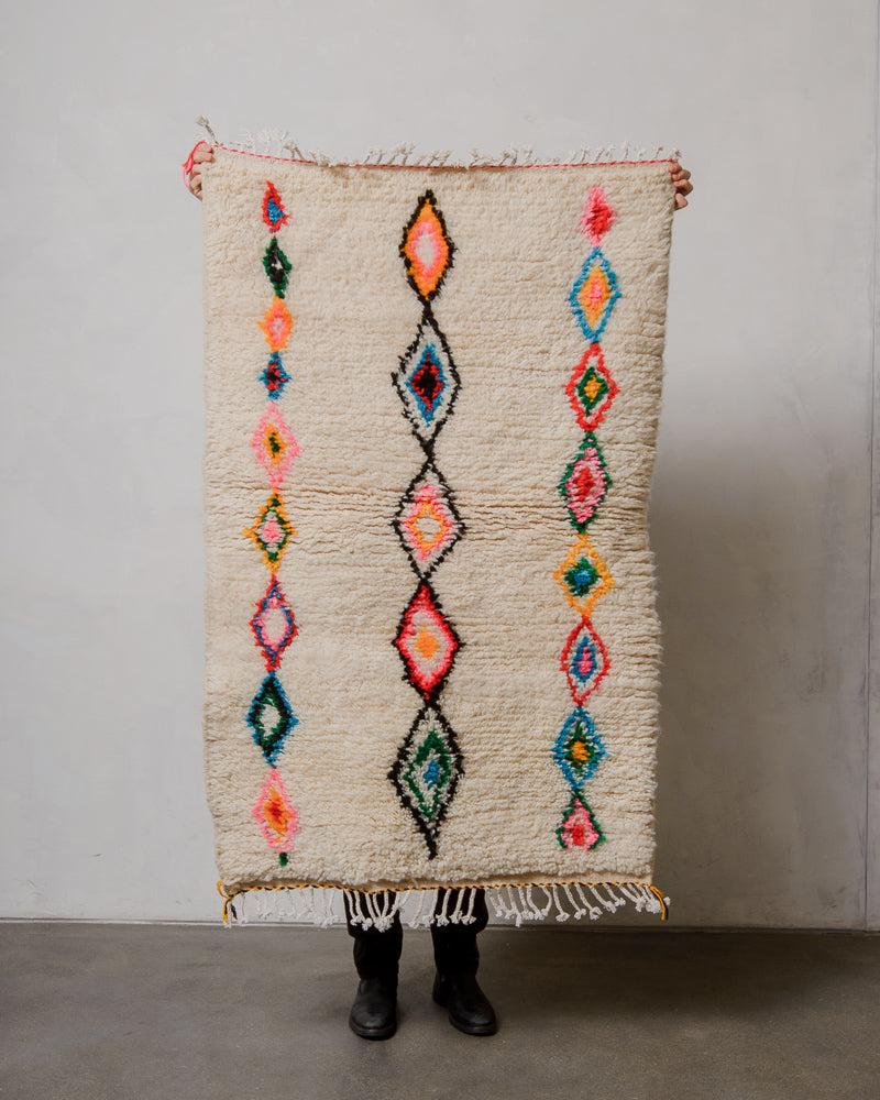 Person holding a colorful patterned rug against a plain wall.