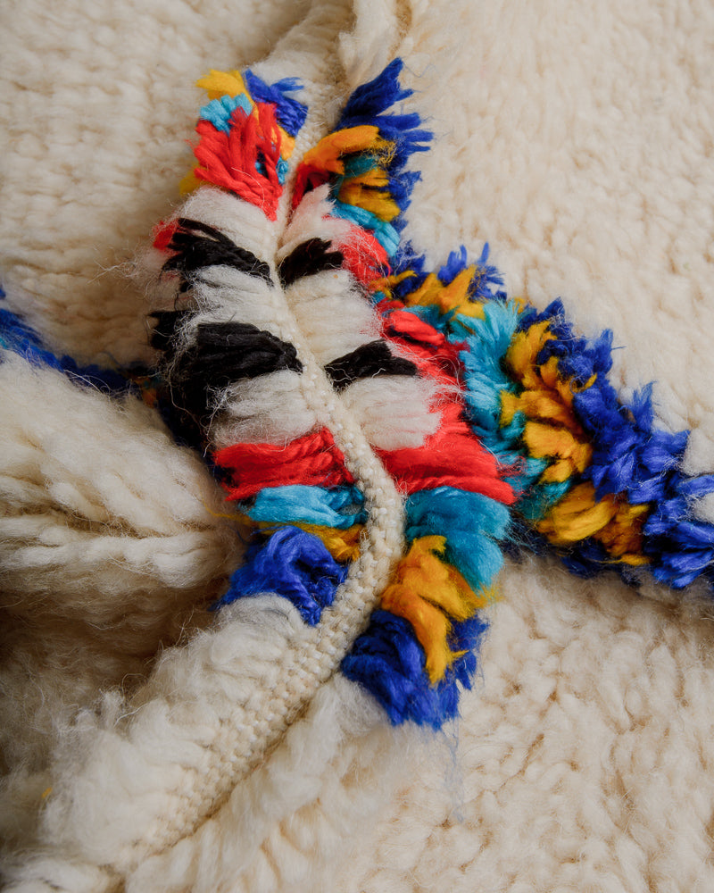 Close up of rug with cream wool and colourful cotton in red, blue, yellow and black