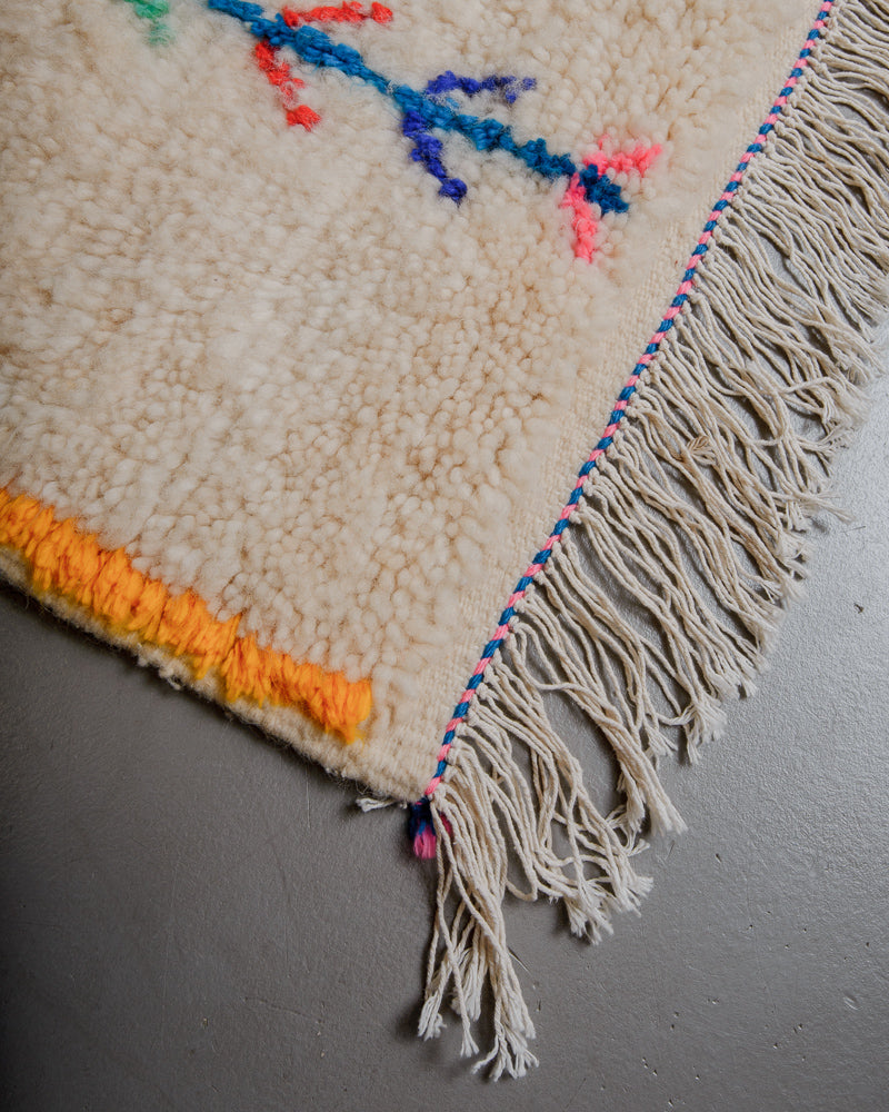 Corner of wool rug with cream wool and colourful cotton accents and white cotton tassels.