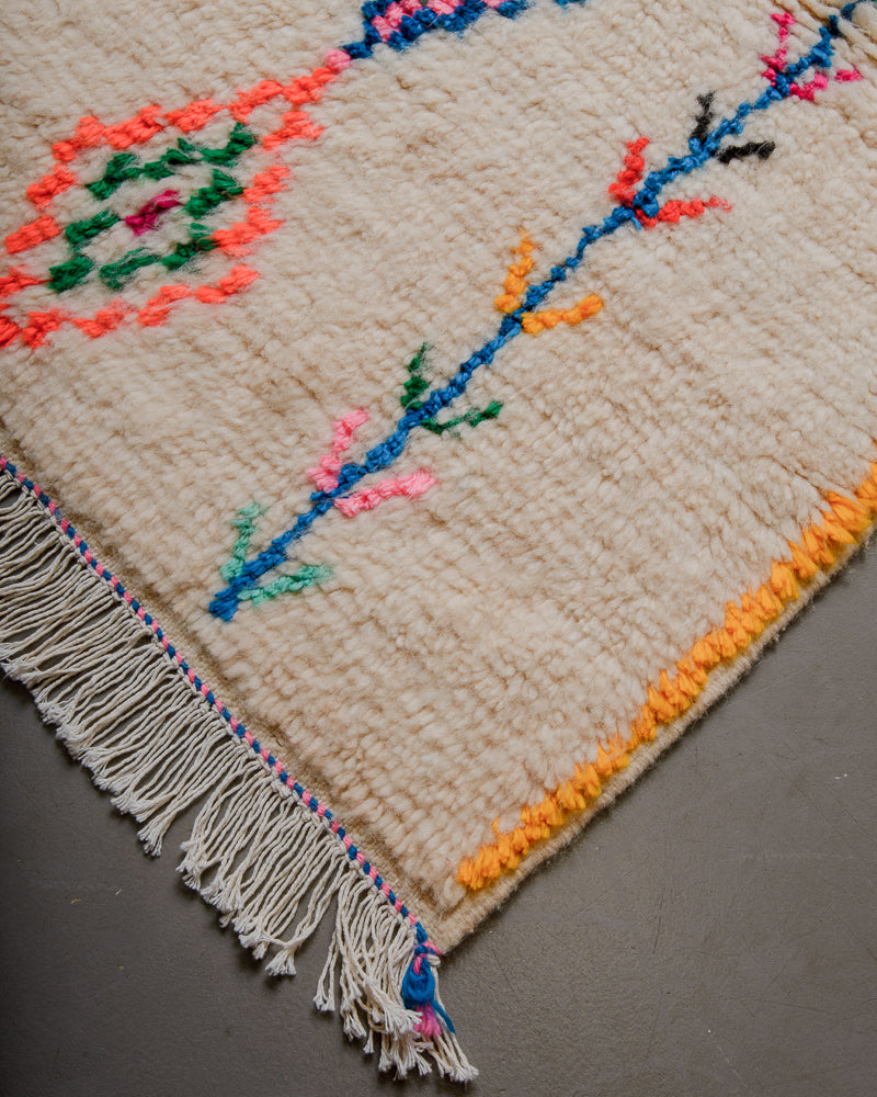 Corner of wool rug with cream wool and colourful cotton accents and white cotton tassels.