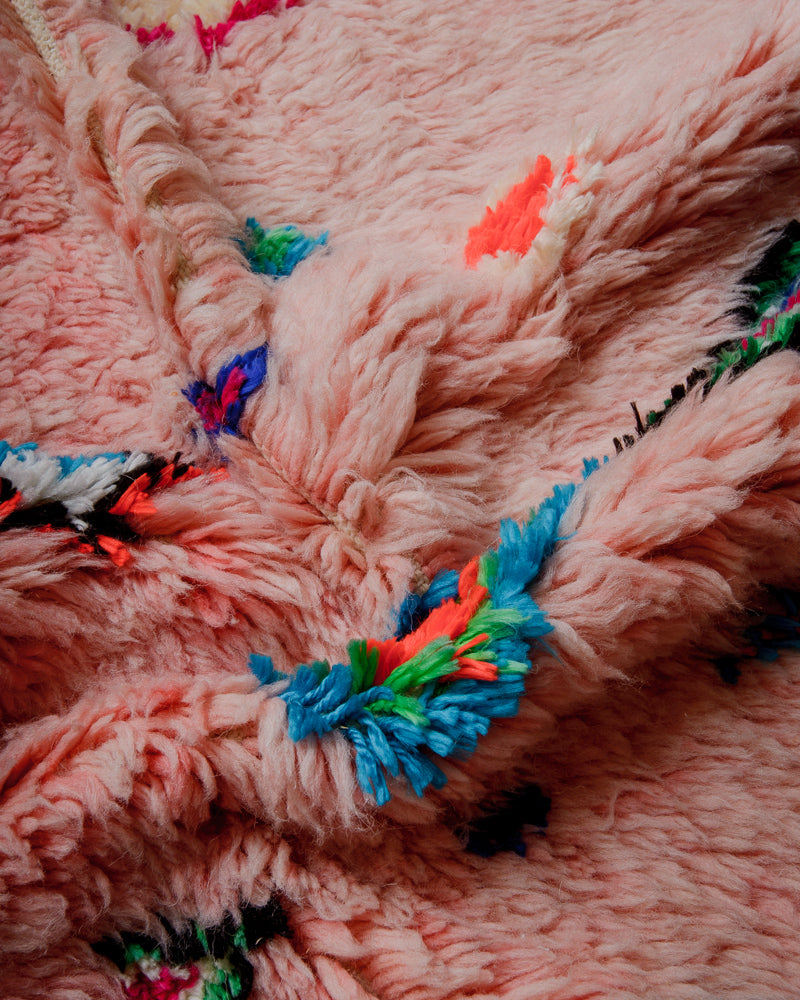 Close up of fluffy pink wool rug with colourful cotton in green, blue, orange and black.