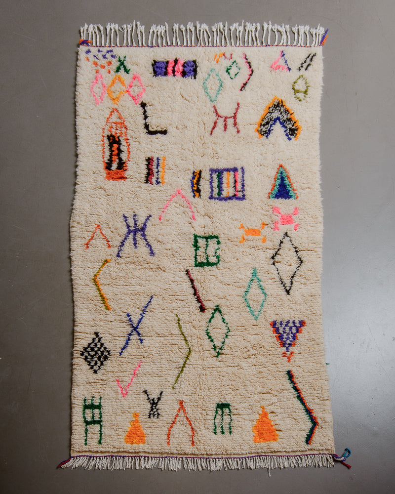 Berberlin Azilal rug with cream wool and colourful cotton flat on grey floor. 