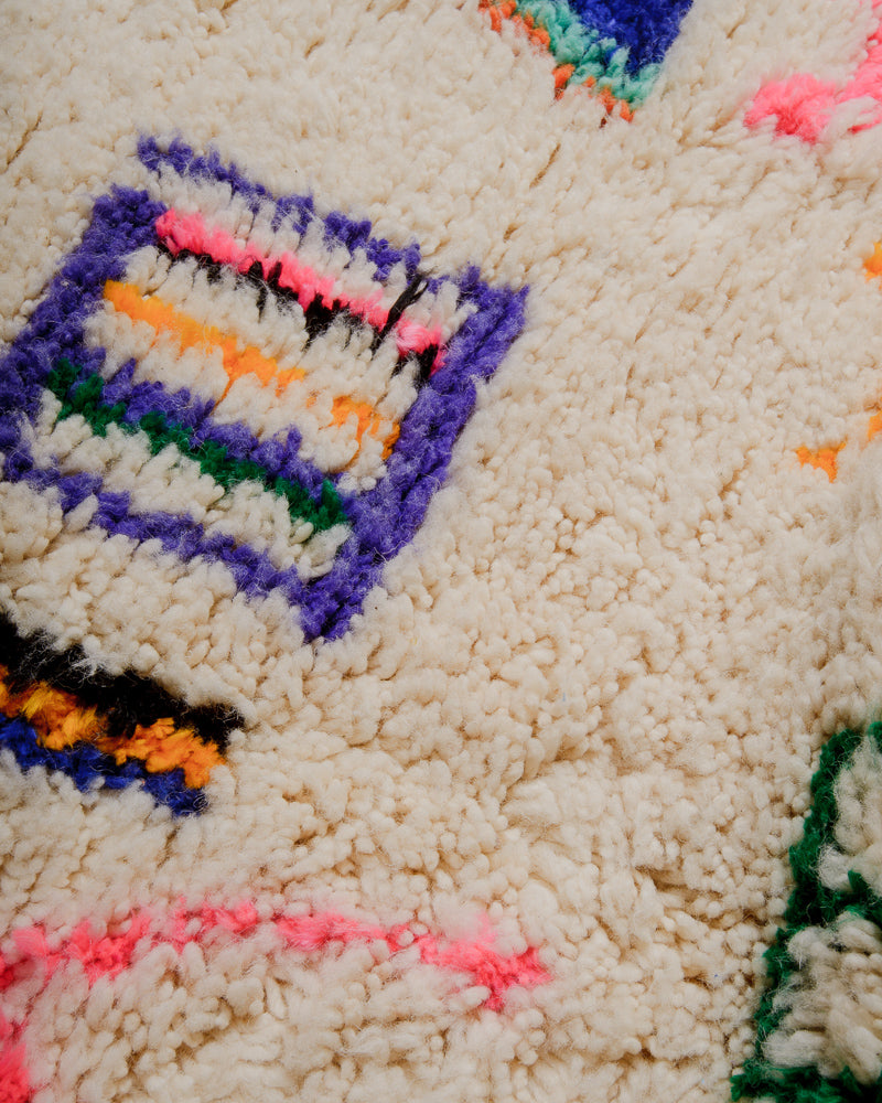 Surface of wool rug with colourful accents in pink, green, orange, and purple.