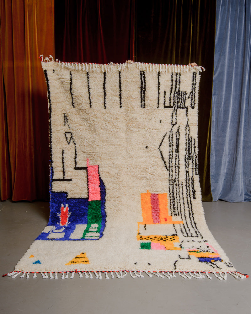 Berberlin Azilal rug with cream wool and colourful cotton being held up in front of velvet curtains.