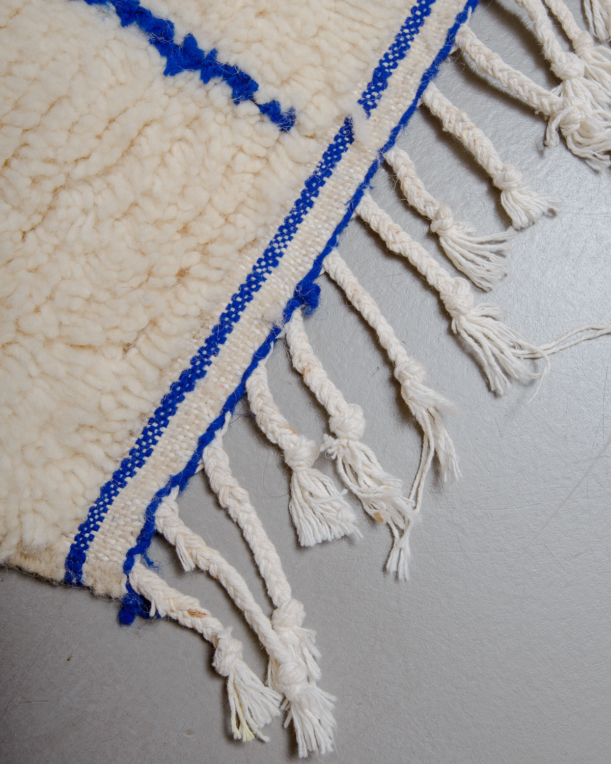 Corner of wool rug with white cotton tassels.