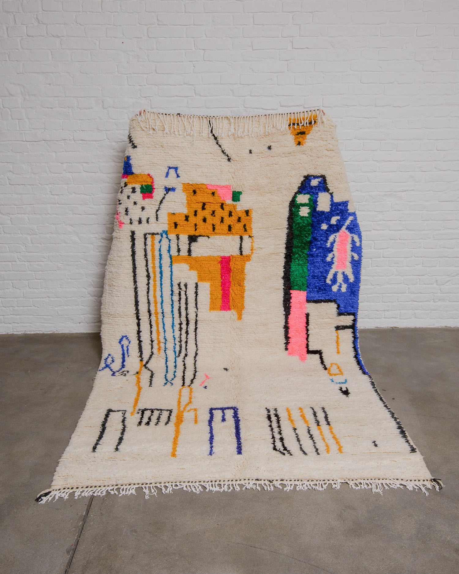 Cream azilal rug with modern, abstract design being held up in front of white brick wall. 