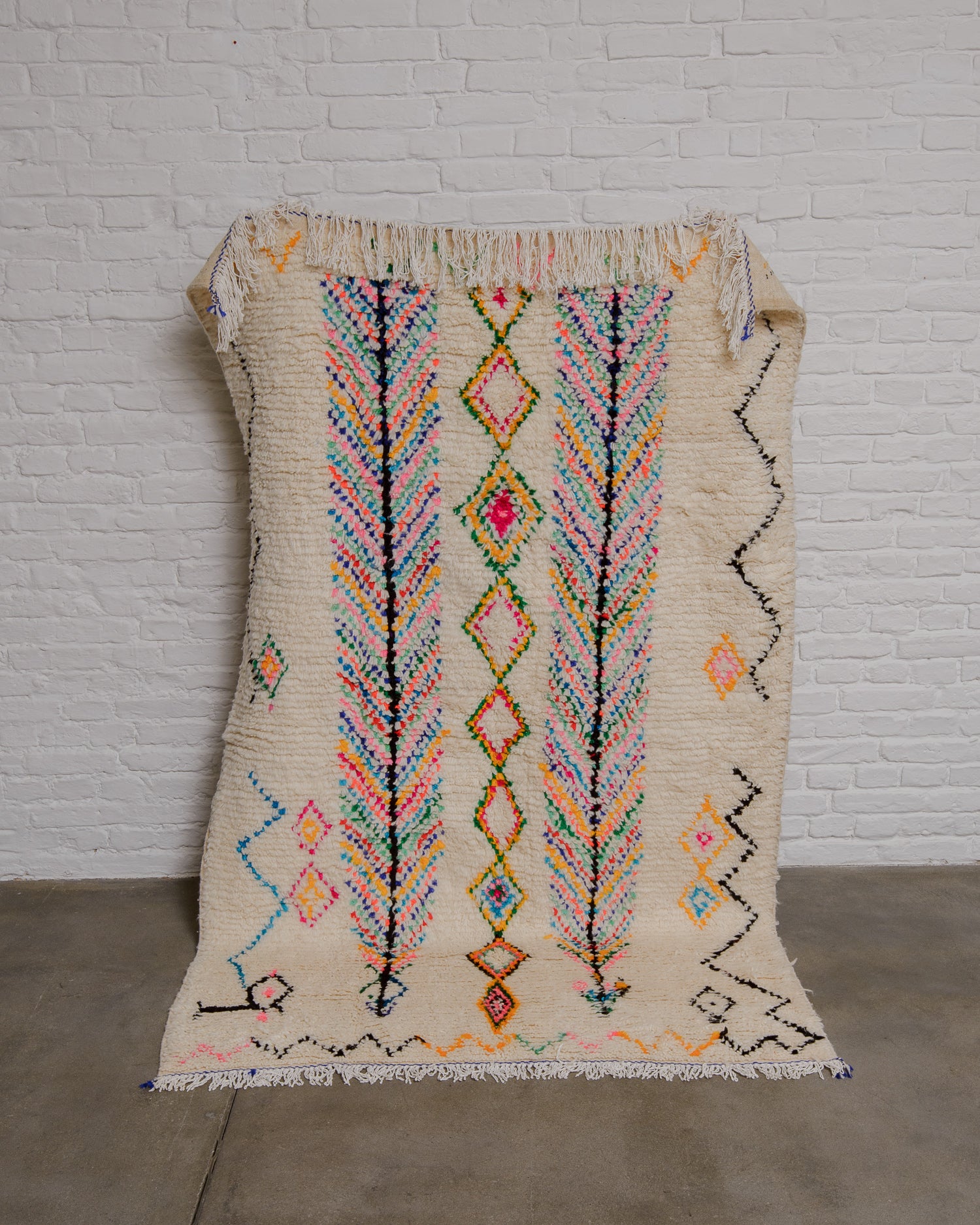 Cream azilal rug with a pattern of confetti colours held up against a white brick wall.