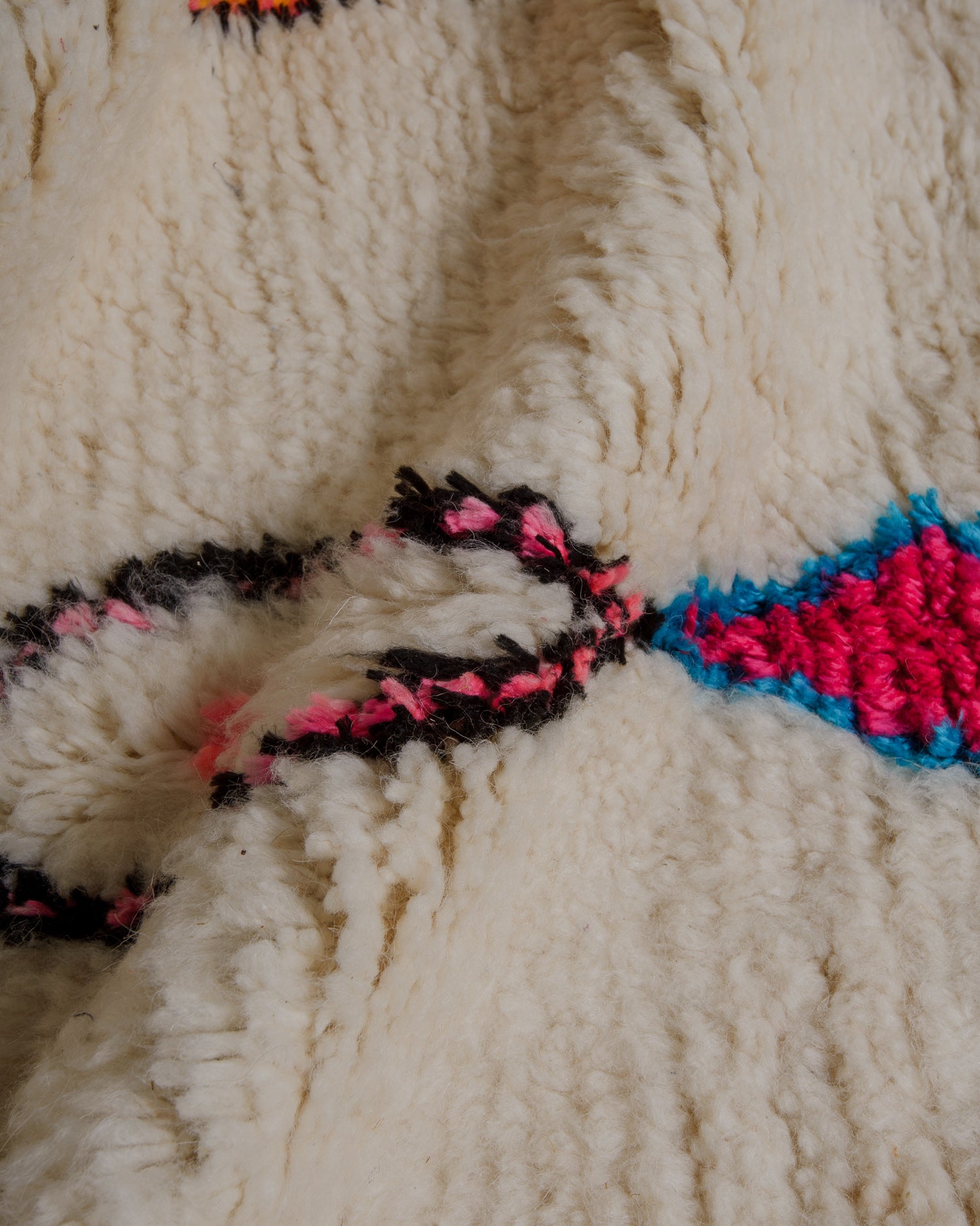 Close up of surface of cream wool azilal rug with design elements in pink, black and blue. 