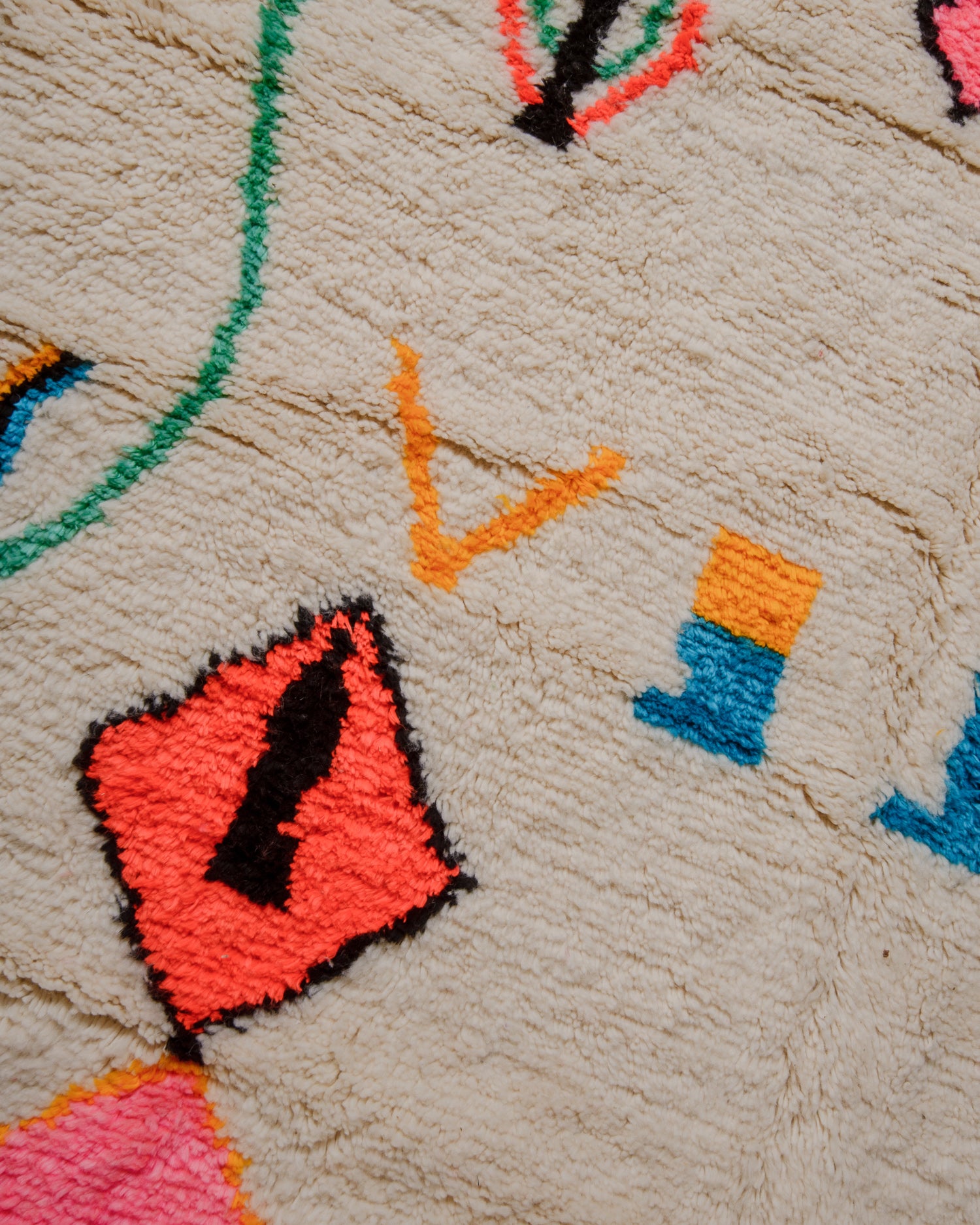 Close up of surface of cream wool azilal rug with brightly coloured design elements.