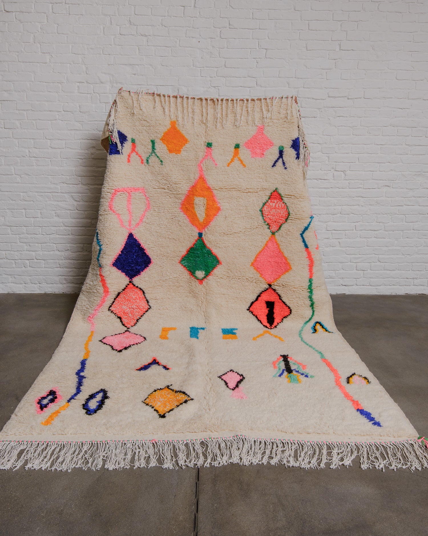 Cream Berberlin Azilal rug with bright colours and bold forms in front of a white wall and cement floor. 