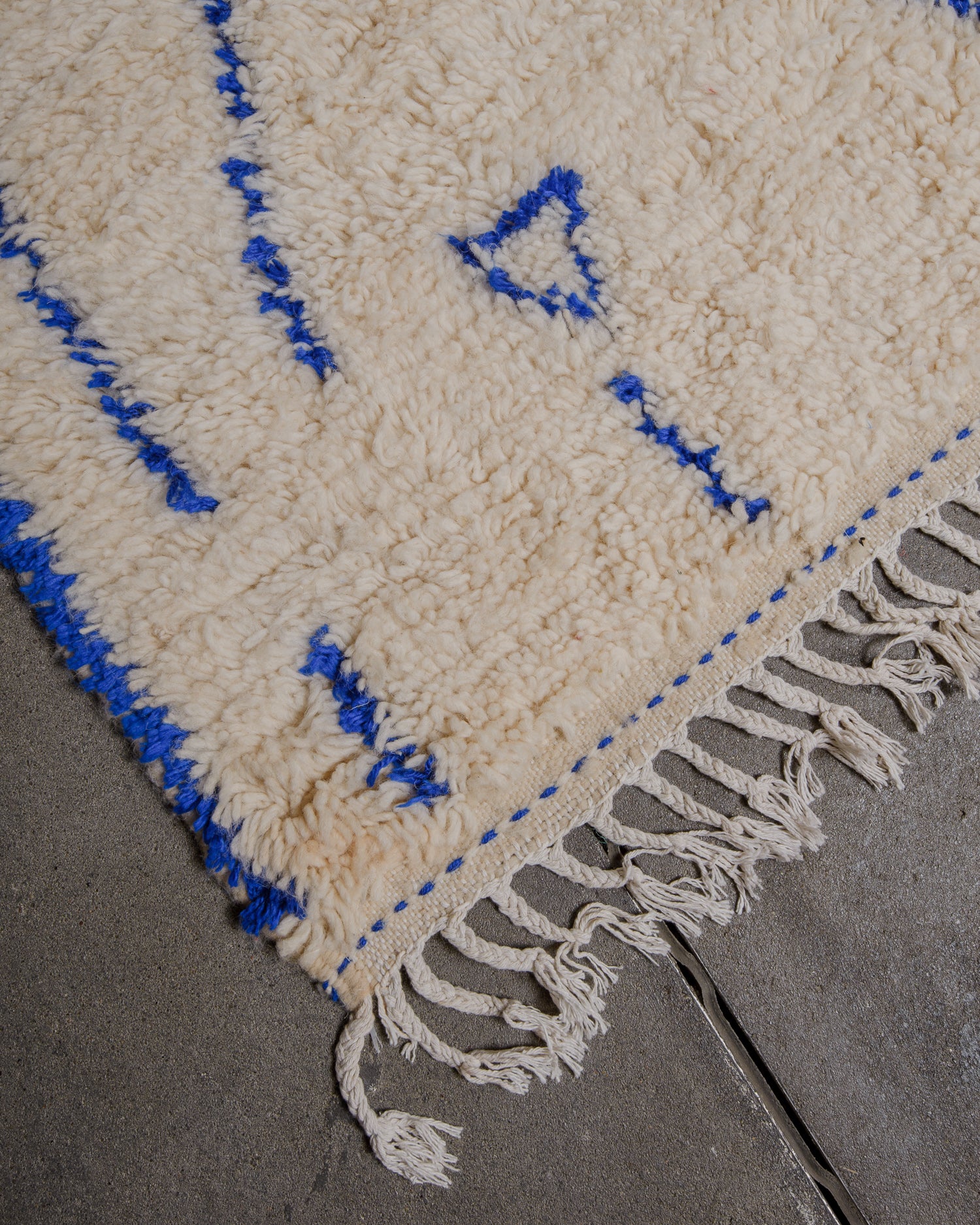 Beige rug with blue accents and white fringe on a gray surface