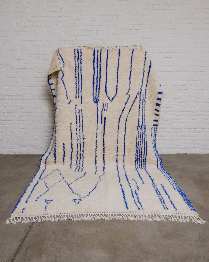 Cream azilal rug with abstract blue lines held in front of a white brick wall.