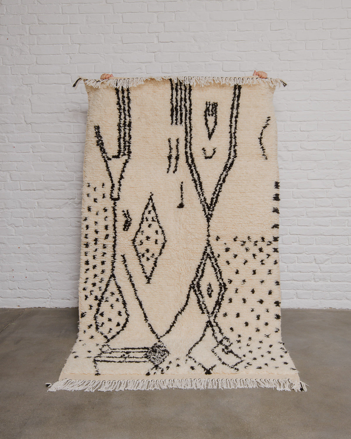 Cream and black patterned rug on a white brick wall background.