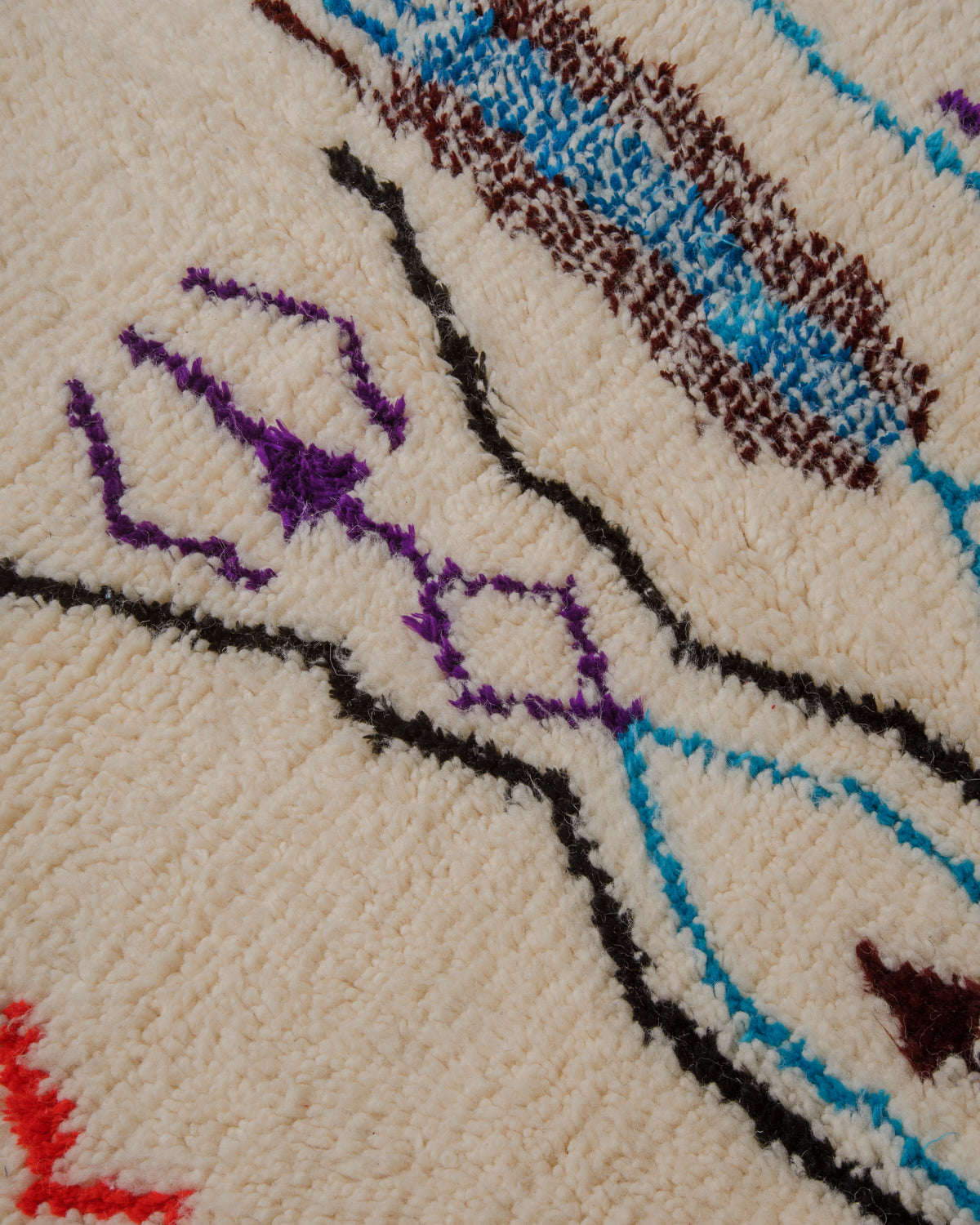 Close up of surface of cream wool rug with design elements in black, purple, blue and brown. 