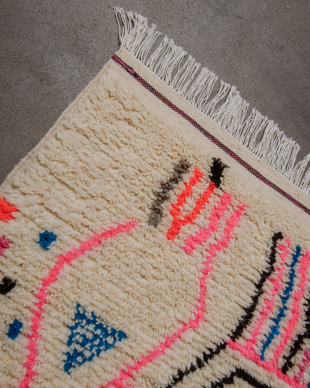 Corner of cream wool Azilal rug with bold pink, orange, blue and grey design elements. 