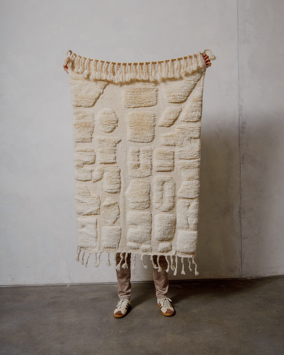 Textured cream rug held by a person against a plain wall.