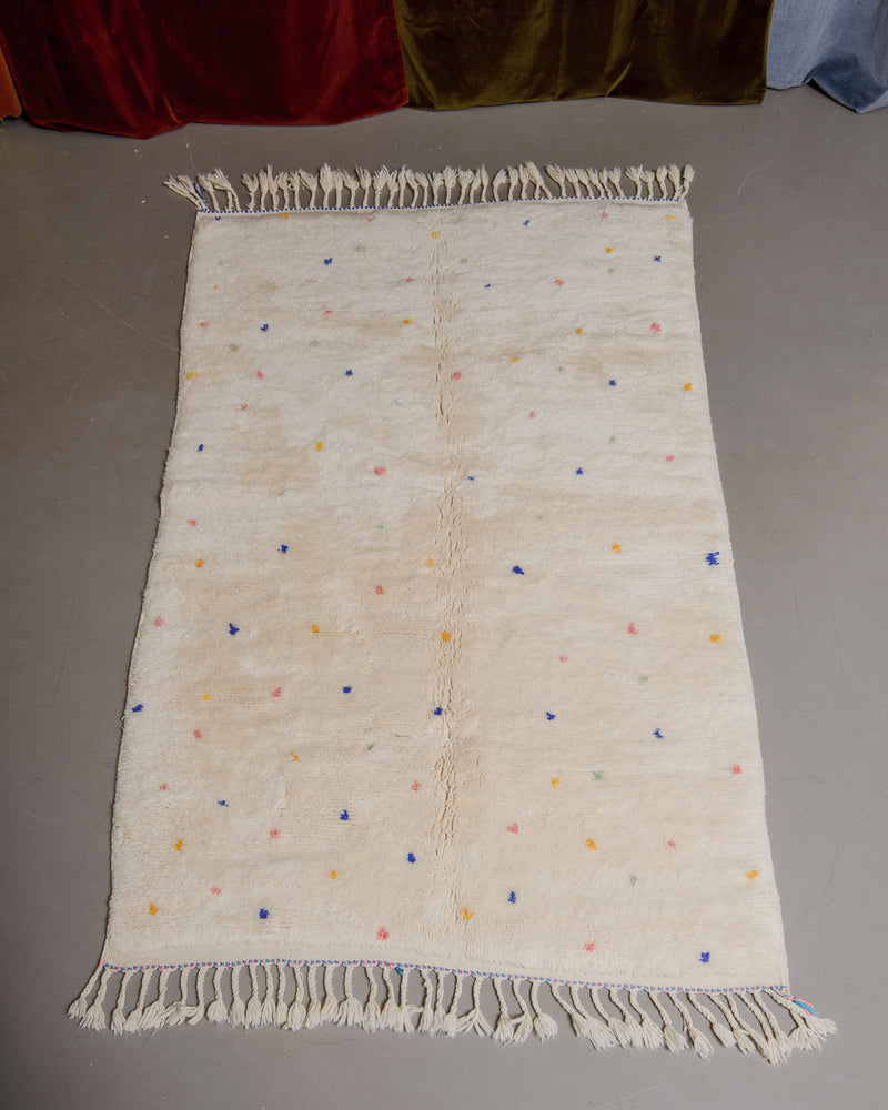 Cream wool rug with colourful polka dots on grey floor. 