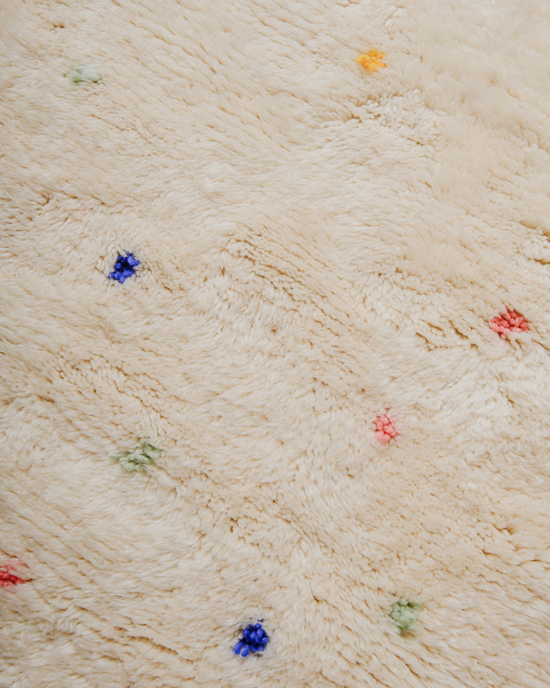 Surface of cream wool rug with colourful dots.