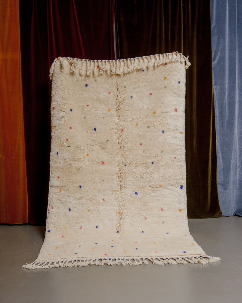Cream wool rug with colourful polka dots in front of velvet curtains.
