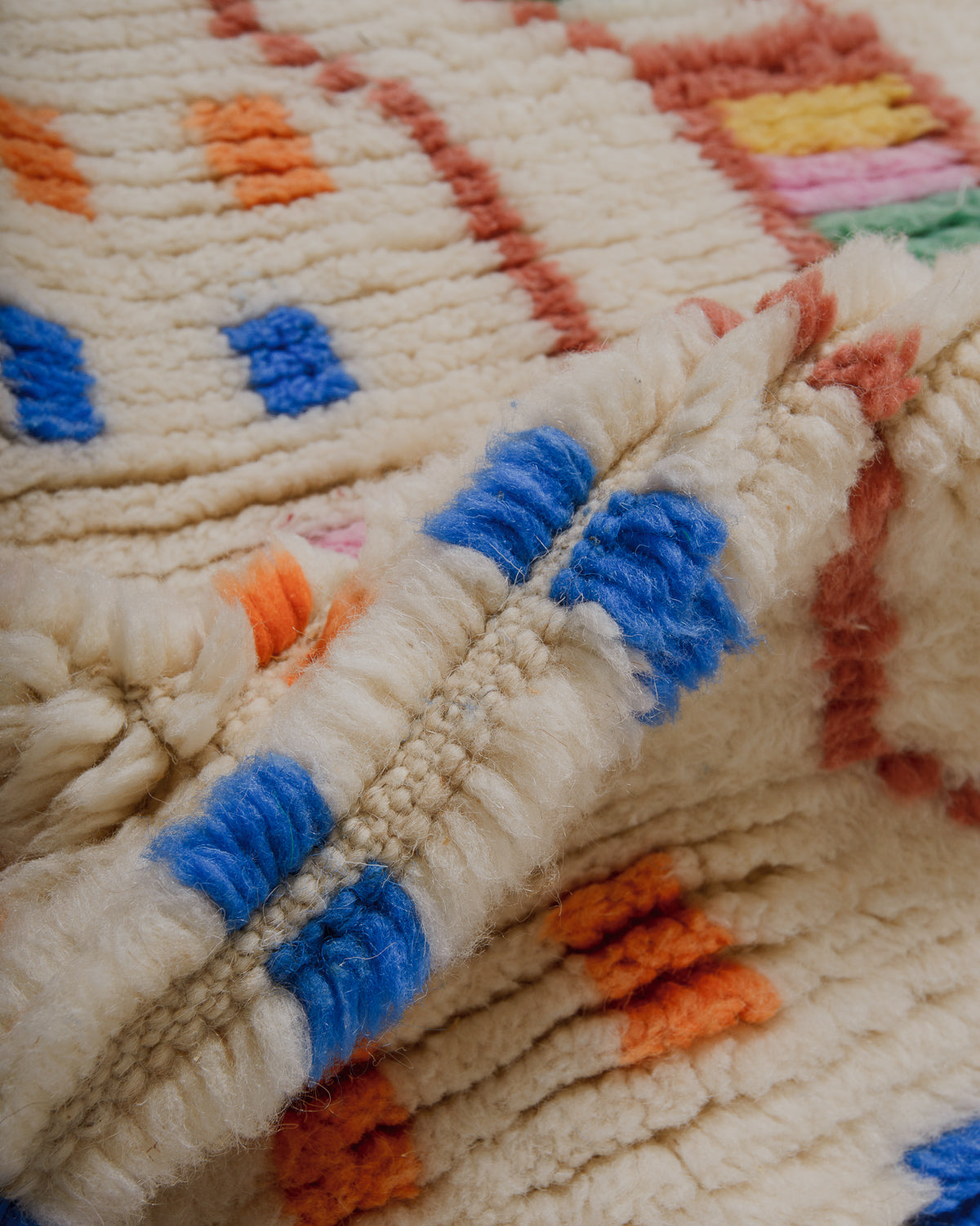 Close-up of wool rug with colourful patterns, featuring blue, orange, brown and pink.