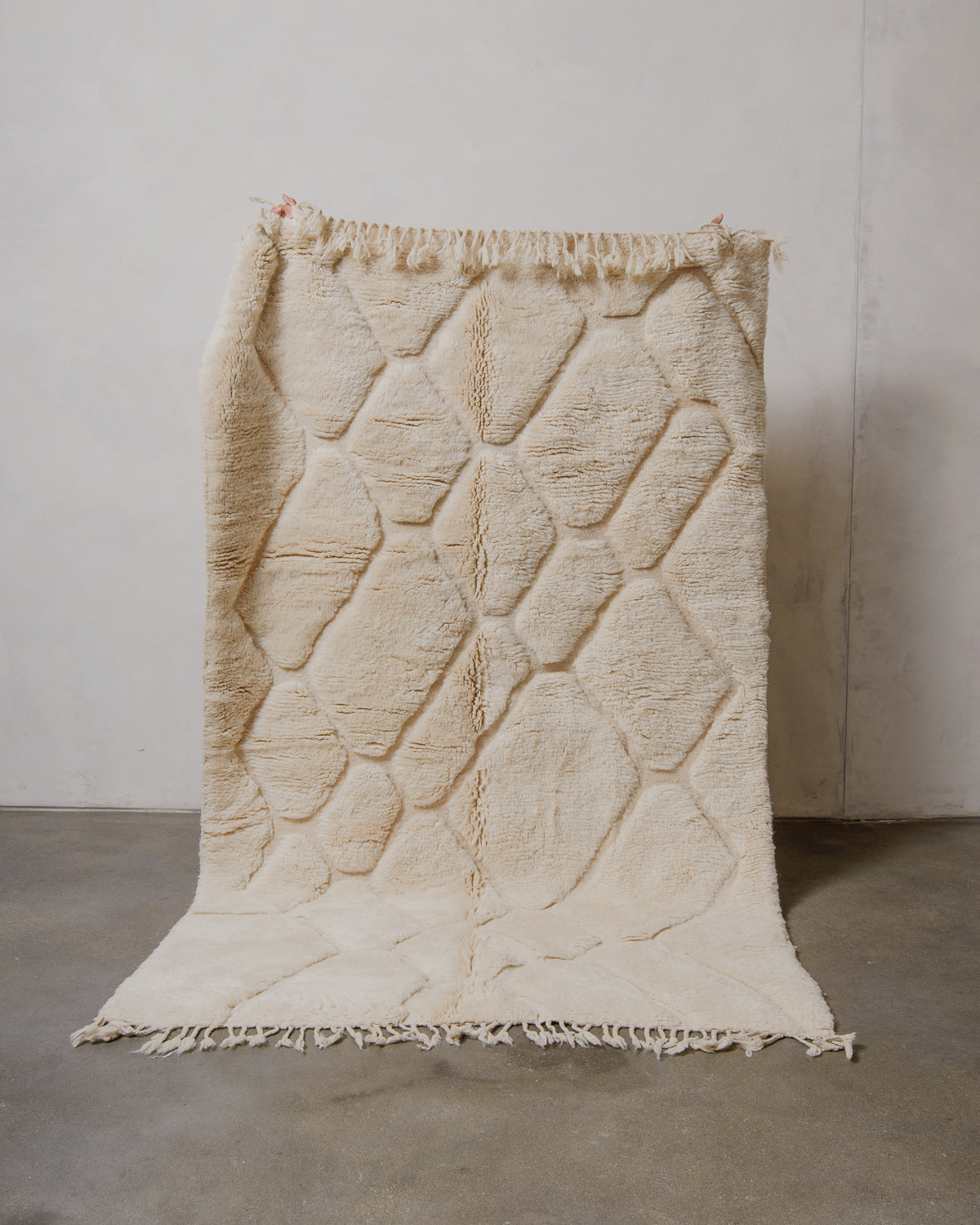 Cream wool rug held up in front of plain white wall. 