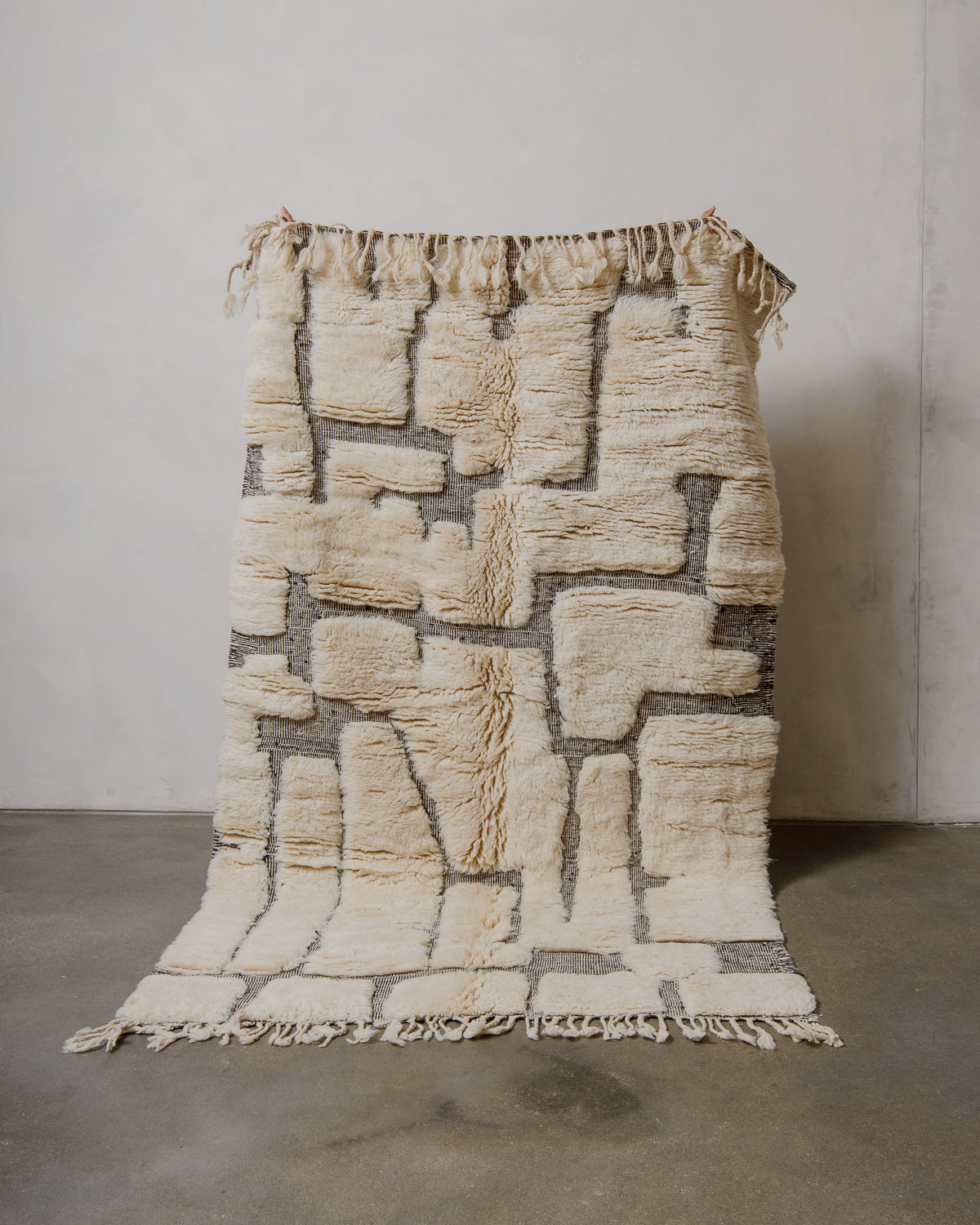 Cream and black wool rug held in front of white wall. 