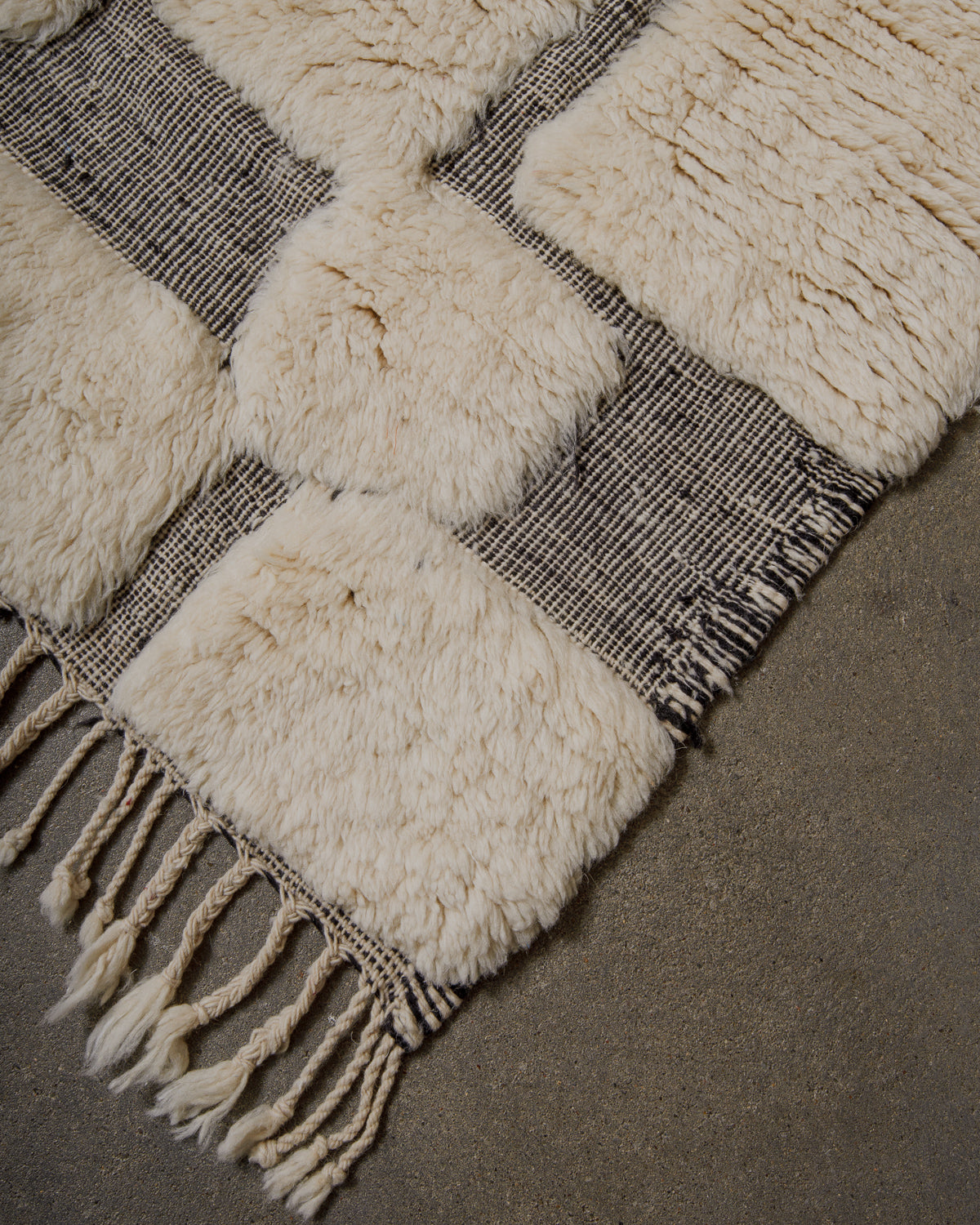 Corner of wool rug with cream knotted areas and flat woven areas in  black and white wool. 
