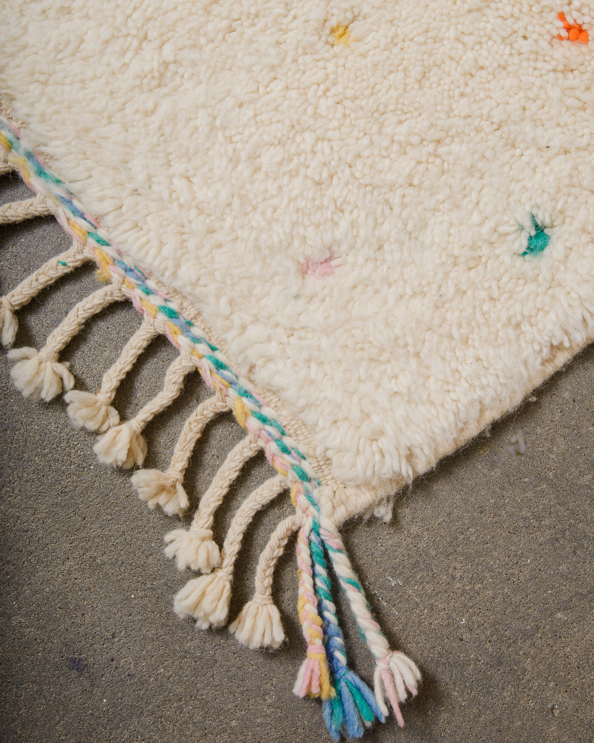 Corner of Berber rug with turquoise, blue, pink and yellow tassels and natural wool tassels across the top.
