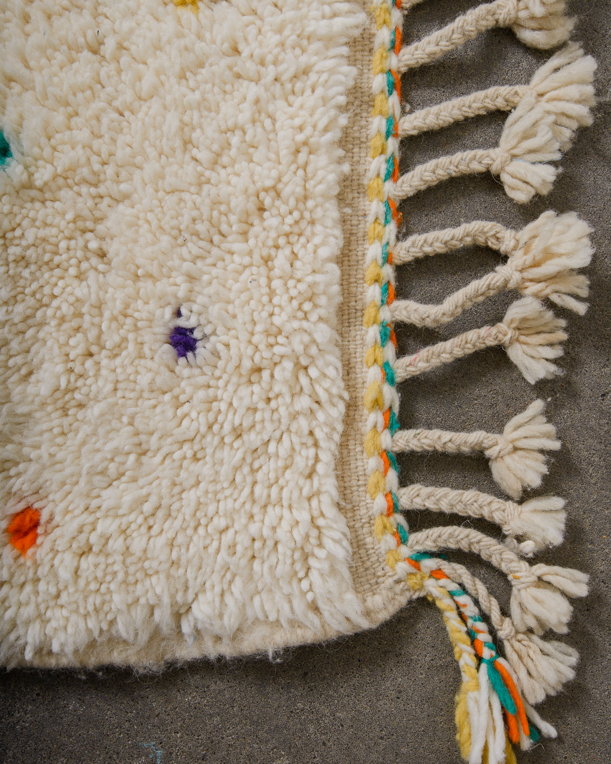 End of Berber rug with turquoise, yellow and orange stitching and natural wool tassels across the top.