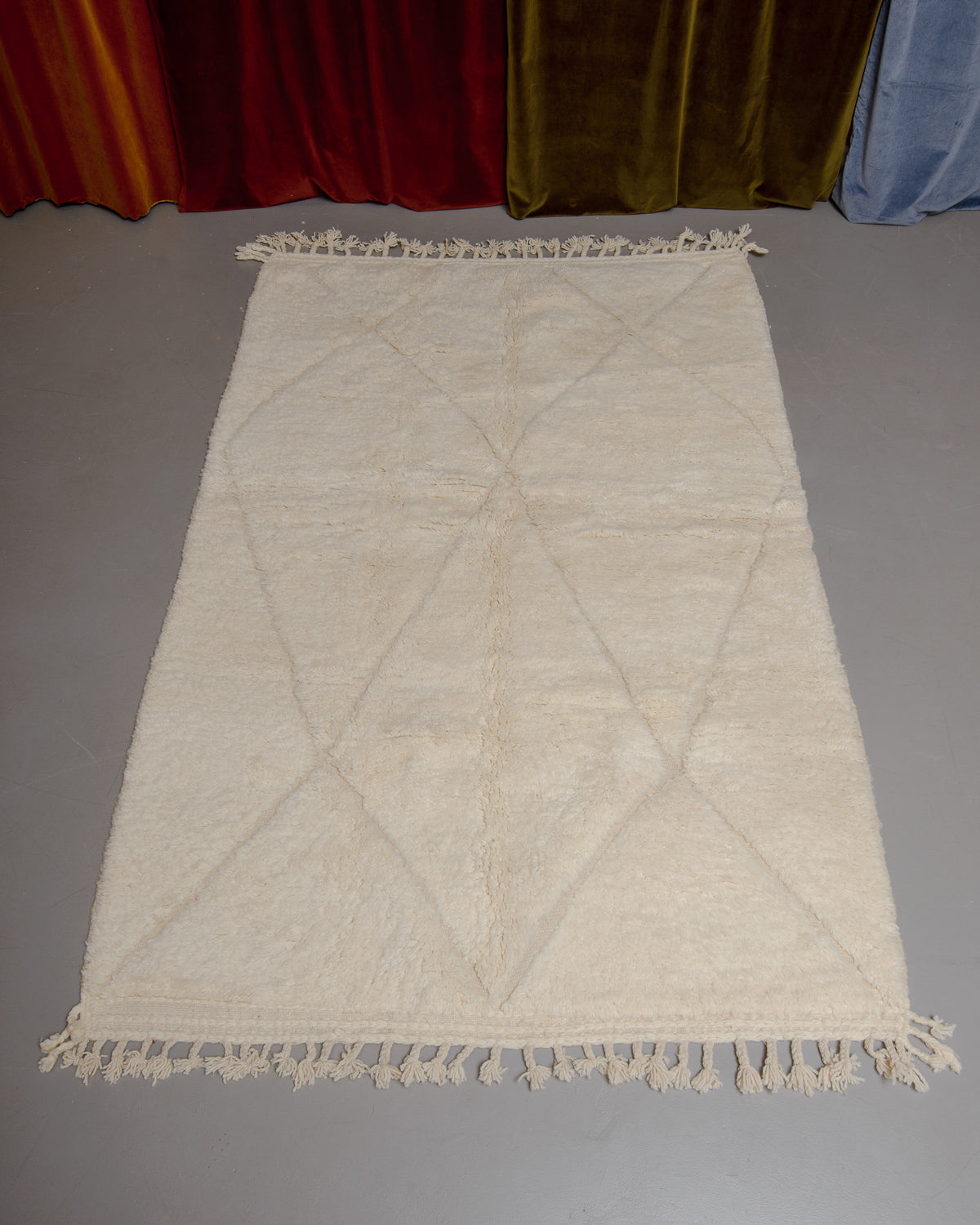 Berberlin Beniourain rug in cream and wool on grey floor in front of velvet curtains.