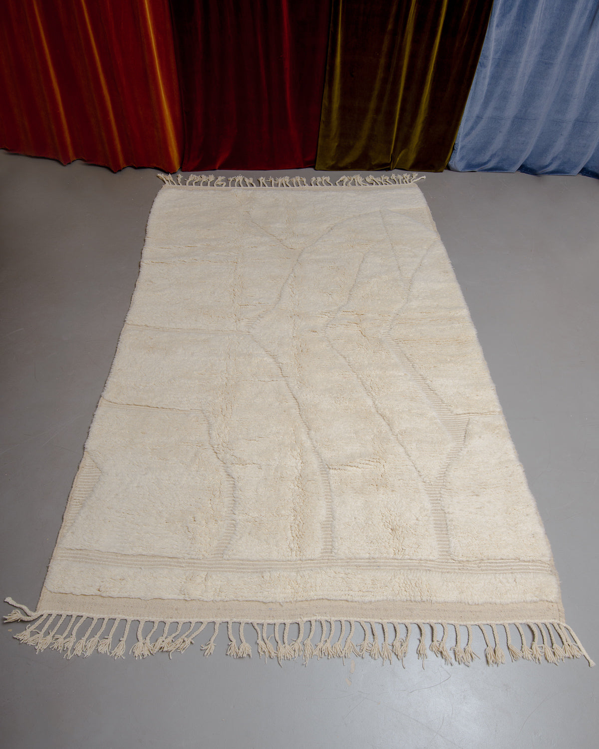 Berberlin Beniourain rug in cream and wool on grey floor in front of velvet curtains.