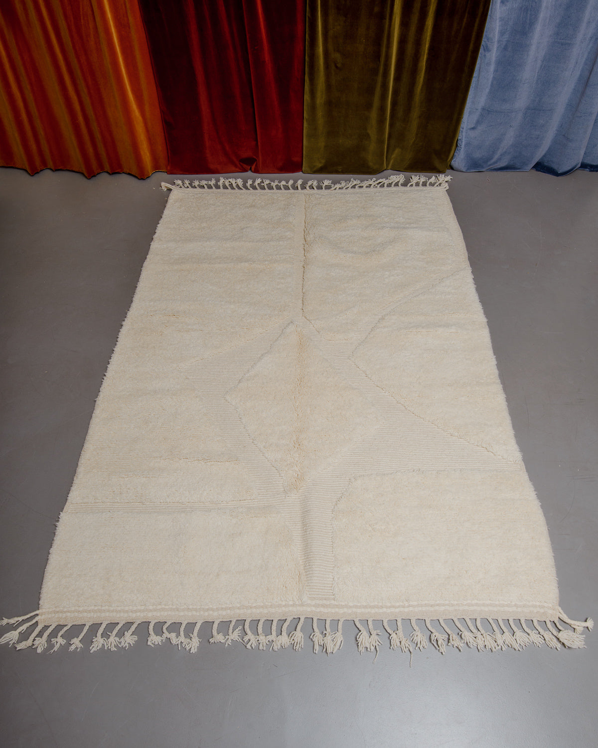 Berberlin Beniourain rug in cream and wool on grey floor in front of velvet curtains.
