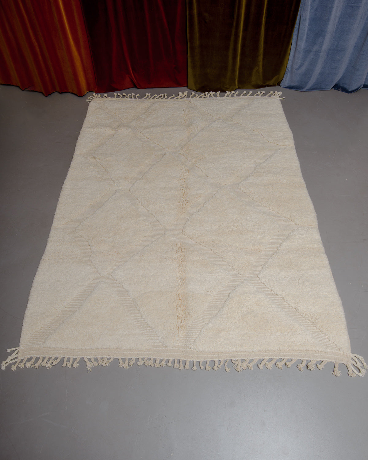 Berberlin Beniourain rug in cream and wool on grey floor in front of velvet curtains.