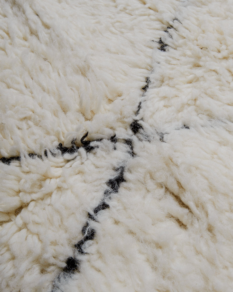Close up of surface of cream wool rug with black lines.